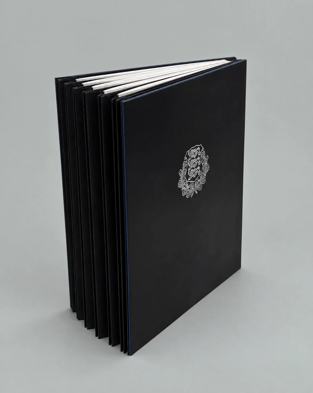 Black leather-covered volume of constitutions standing upright, a silver coat of arms on the front cover